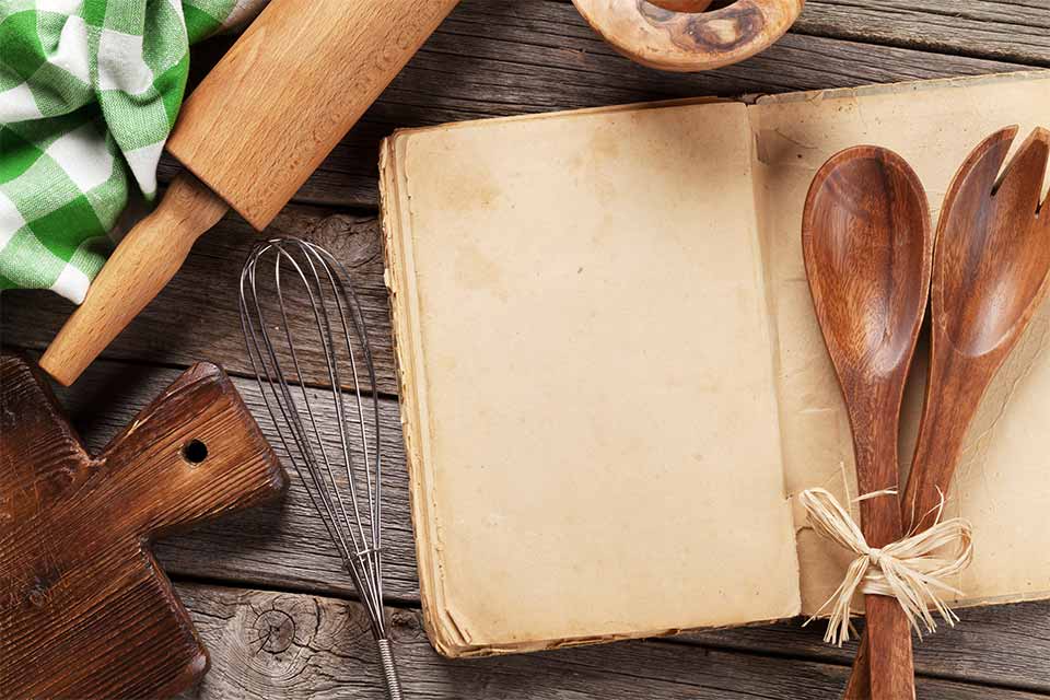 Recipe book surrounded by a rolling pin, cutting board and kitchen towel.