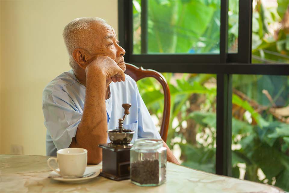 Elderly man with depression looking forlorn, staring out window.