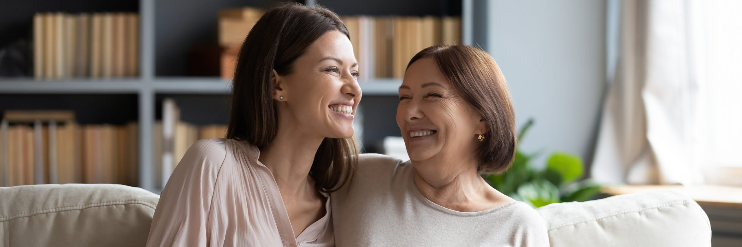 Senior mom and daughter sitting on couch smiling