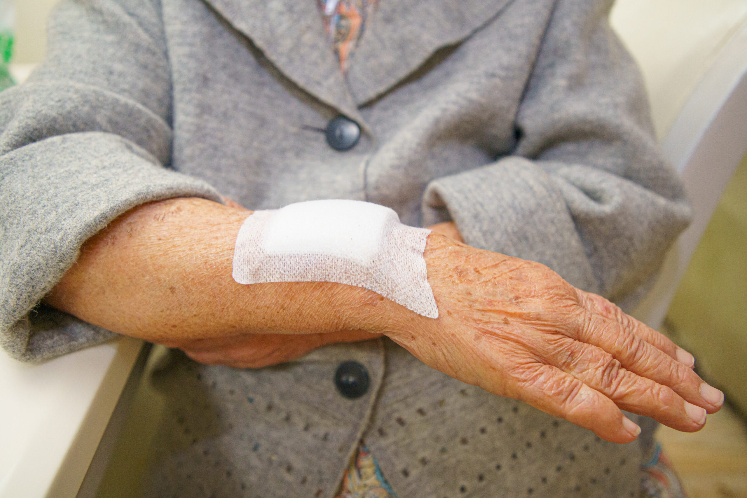 An elderly woman in a coat wear a bandage on her arm.