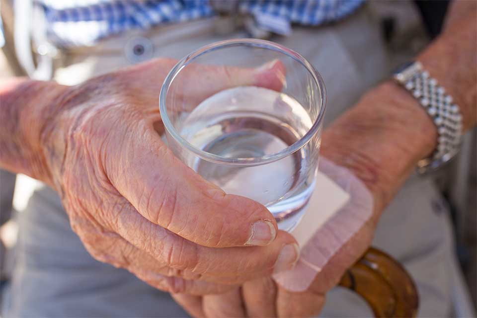 Elderly man with a bandage on his hand holding a glass of water