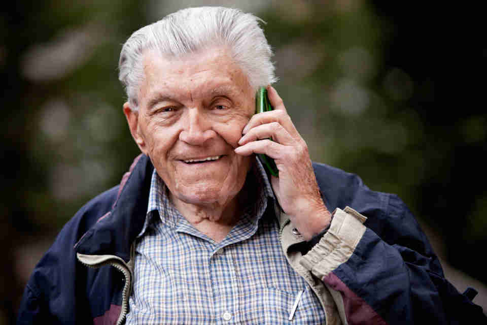 Elderly man in navy blue jacket talking on cell phone.