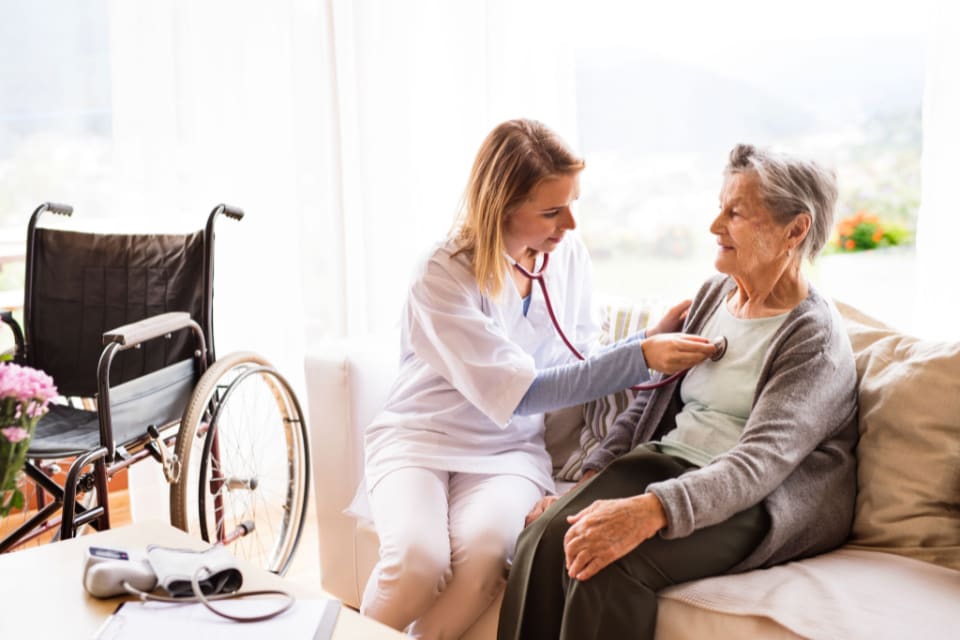 An in-home caregiver uses a stethoscope on a senior woman