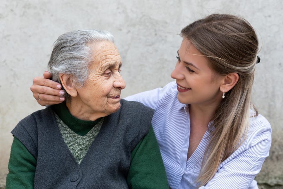 Younger woman sitting with her arm around the shoulders of an elderly woman.