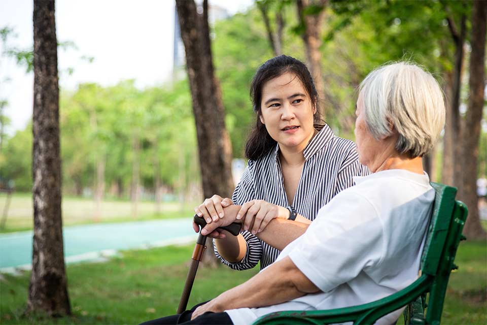 Elderly woman and her daughter caregiver sitting on a bench in the park.