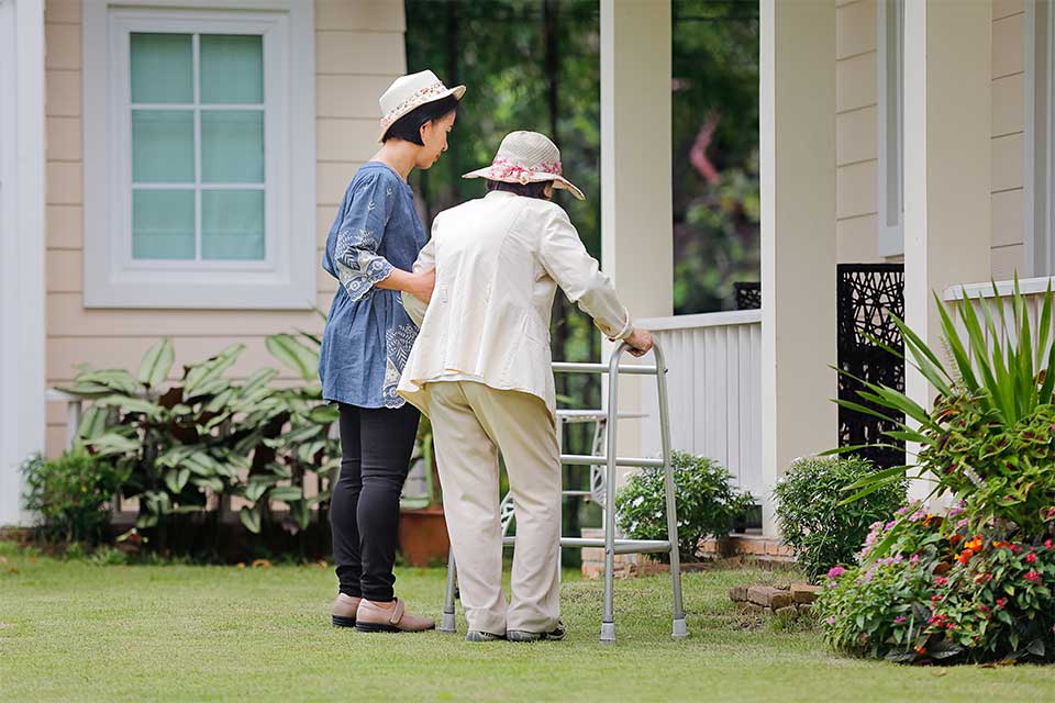 Caregiver helping elderly woman with a walker get to the front door of her house