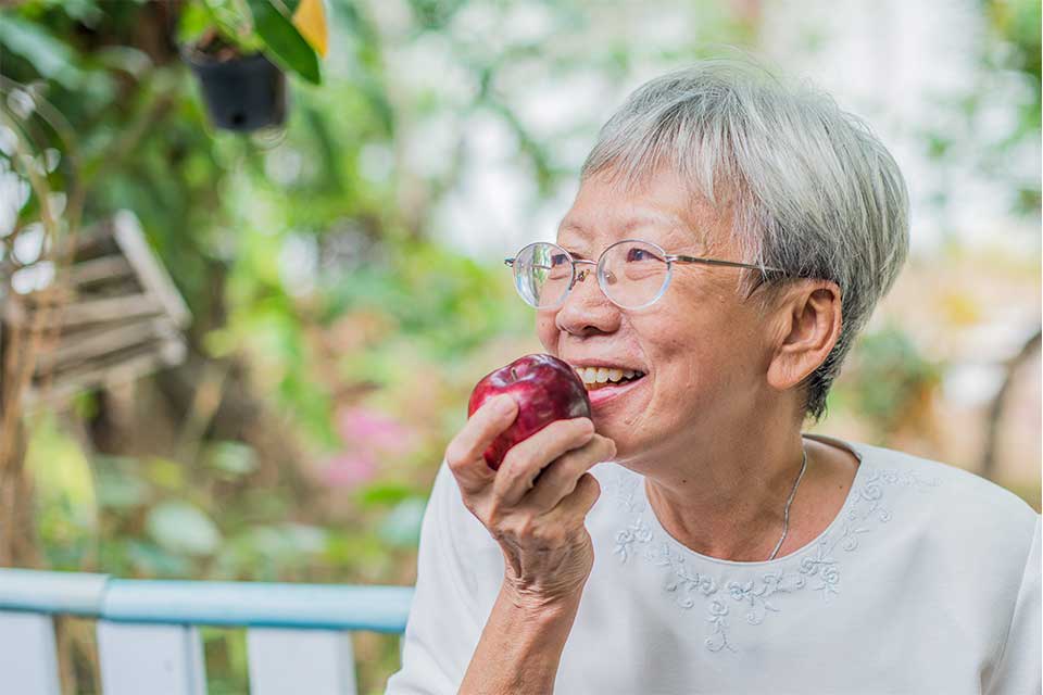 Elderly woman getting ready to take a bit of a red apple.