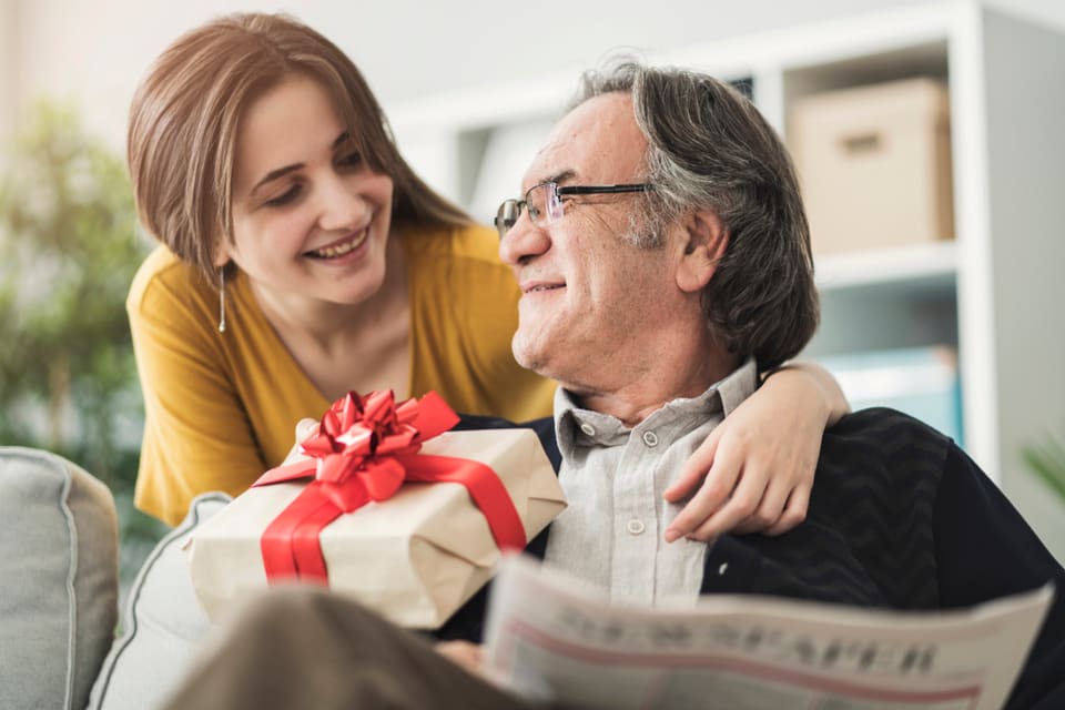 Younger woman giving a seated older man a gift.