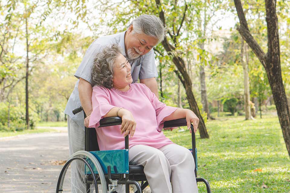 Male caregiver taking his female patient for a walk in her wheelchair in the park.