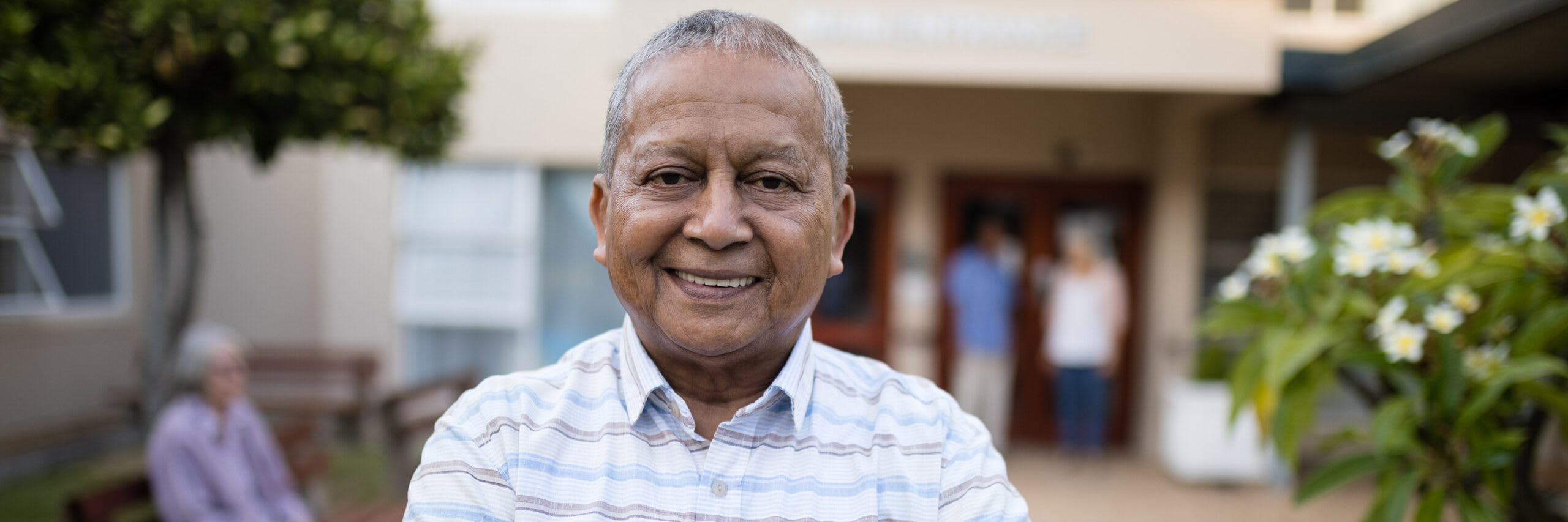 A senior smiling while standing in front of a nursing home