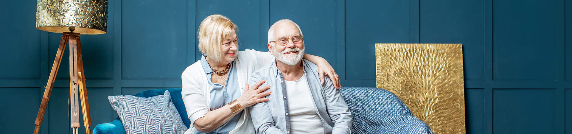 A senior couple smiles as they embrace on the couch