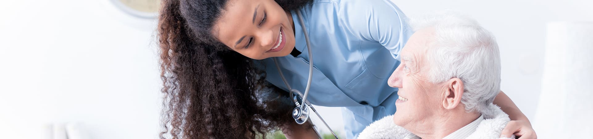 A caregiver with a stethoscope smiles at a senior as she puts her arm around his shoulder