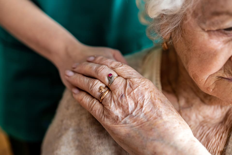 Older woman looking down while holding a younger woman's hand on her shoulder.