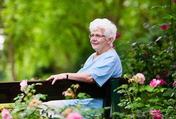 A senior woman sitting on a park bench amidst flowers
