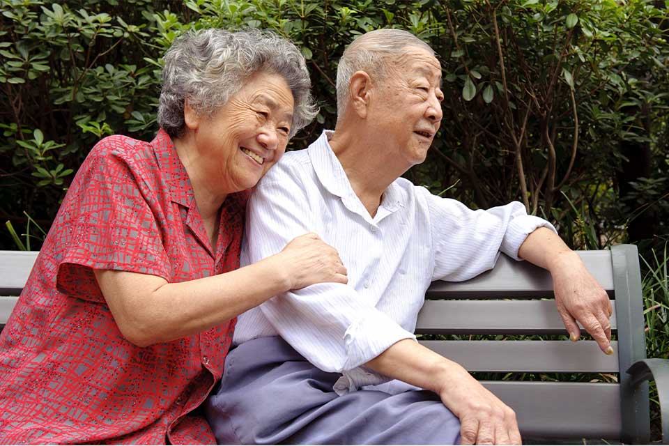 Elderly couple sitting on a park bench near their senior living community.