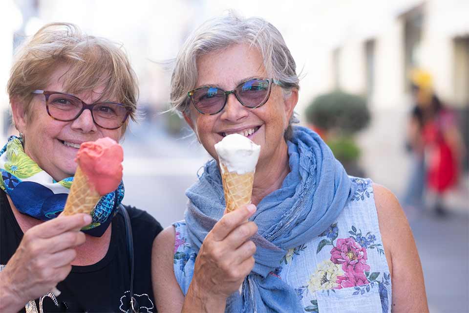 Two senior women smile while holding ice cream cones.