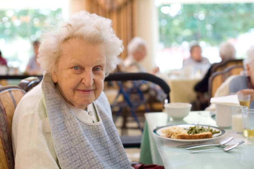 A senior woman smiling, seated at a dining table