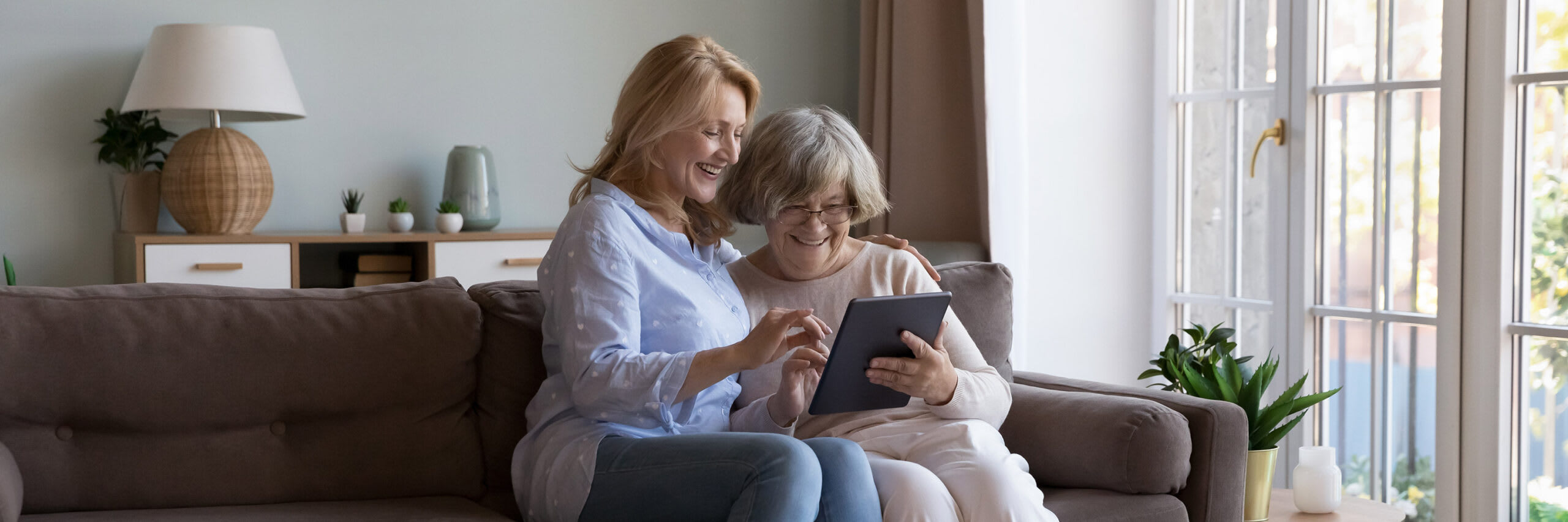 Senior and daughter looking at a tablet together smiling on the couch