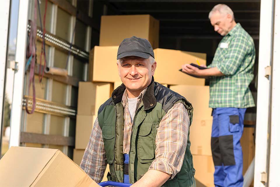 A senior man sits on the edge of a moving truck.