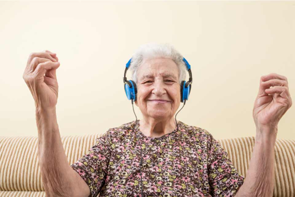 Elderly woman wearing headphones, listening to music and moving her arms to its rhythm.
