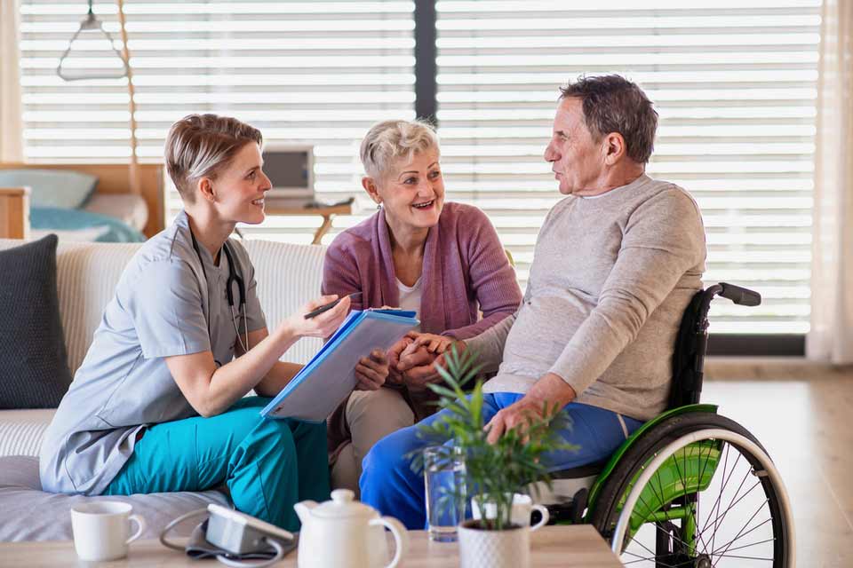 Elderly man in a wheelchair and elderly woman talking to their nurse in a nursing home.