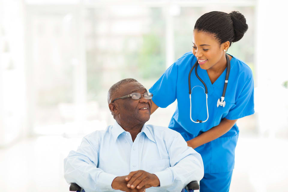 Young black woman looking at older black man while pushing him in a wheelchair.
