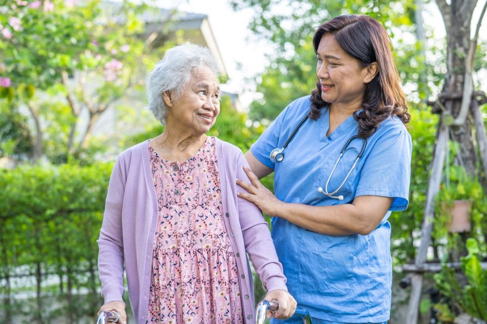 A caregiver and resident walking outside is an example of person centered memory care management.