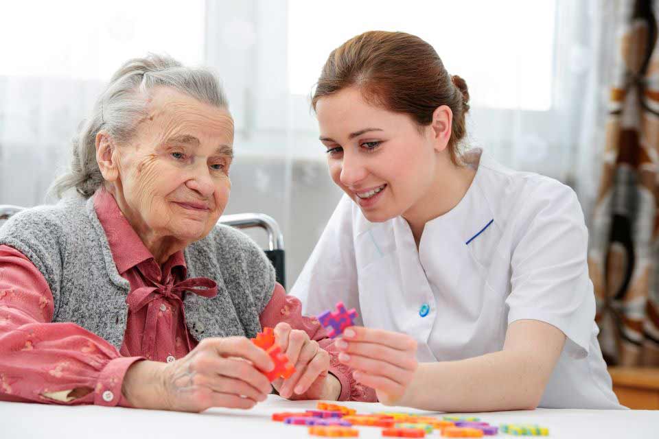 A caregiver at a memory care facility sits with a resident.