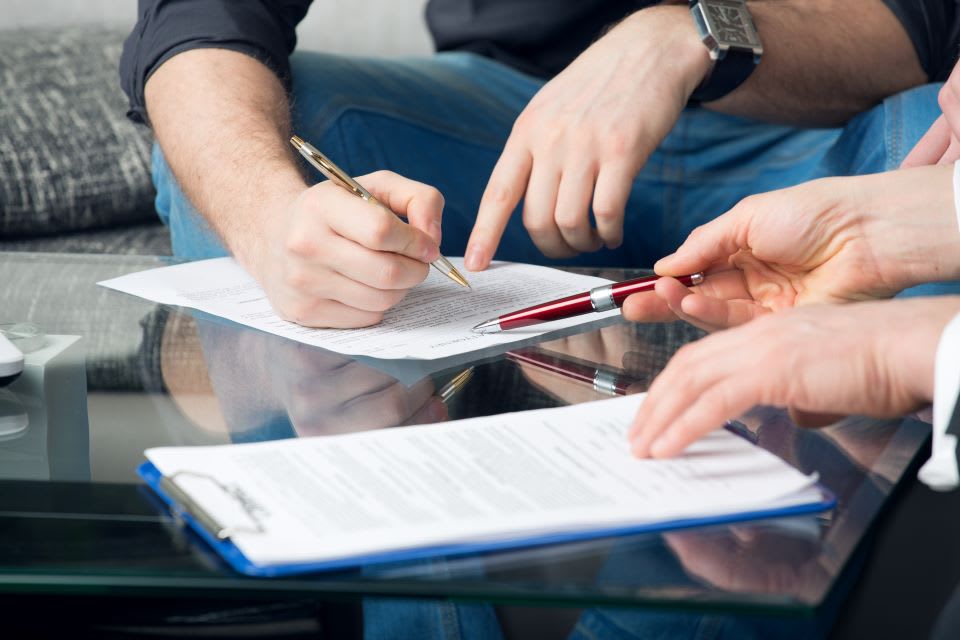 Hands of two people signing paperwork.