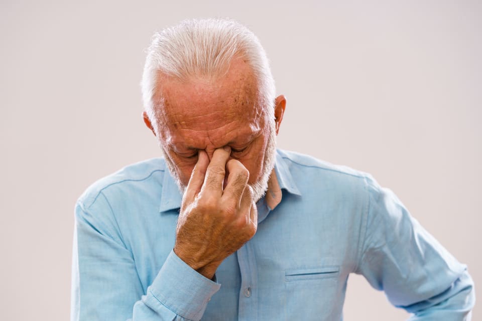 Older man in blue shirt has a headache, touching head.