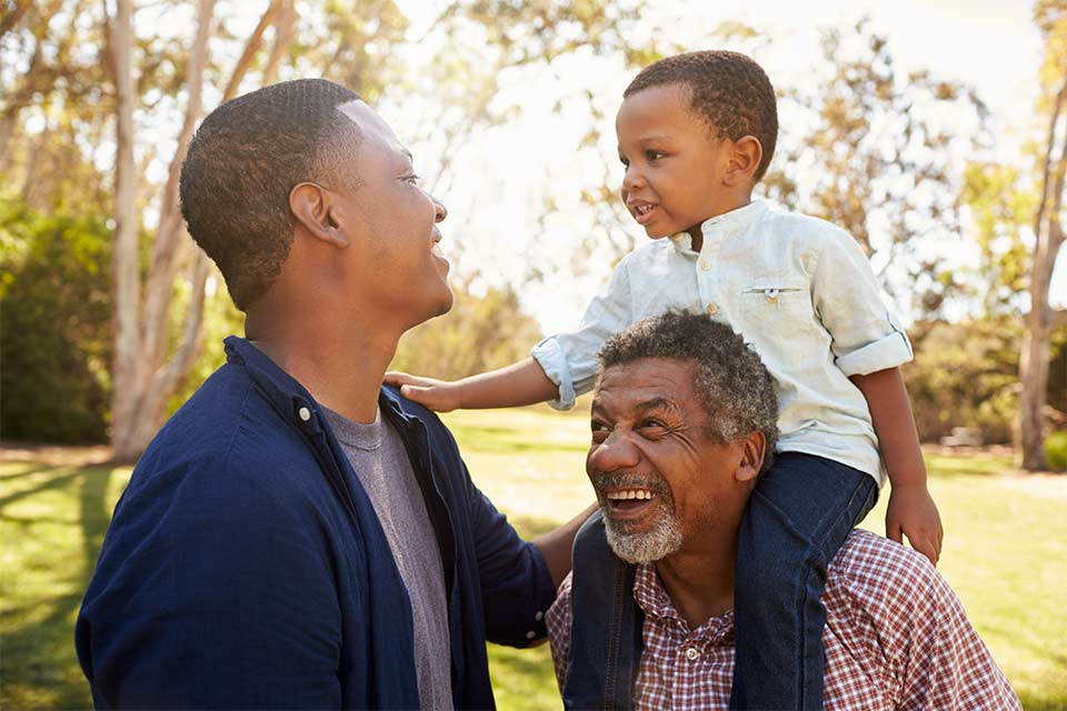 Three generations of men laughing together in a park, otherwise known as the sandwich generation.