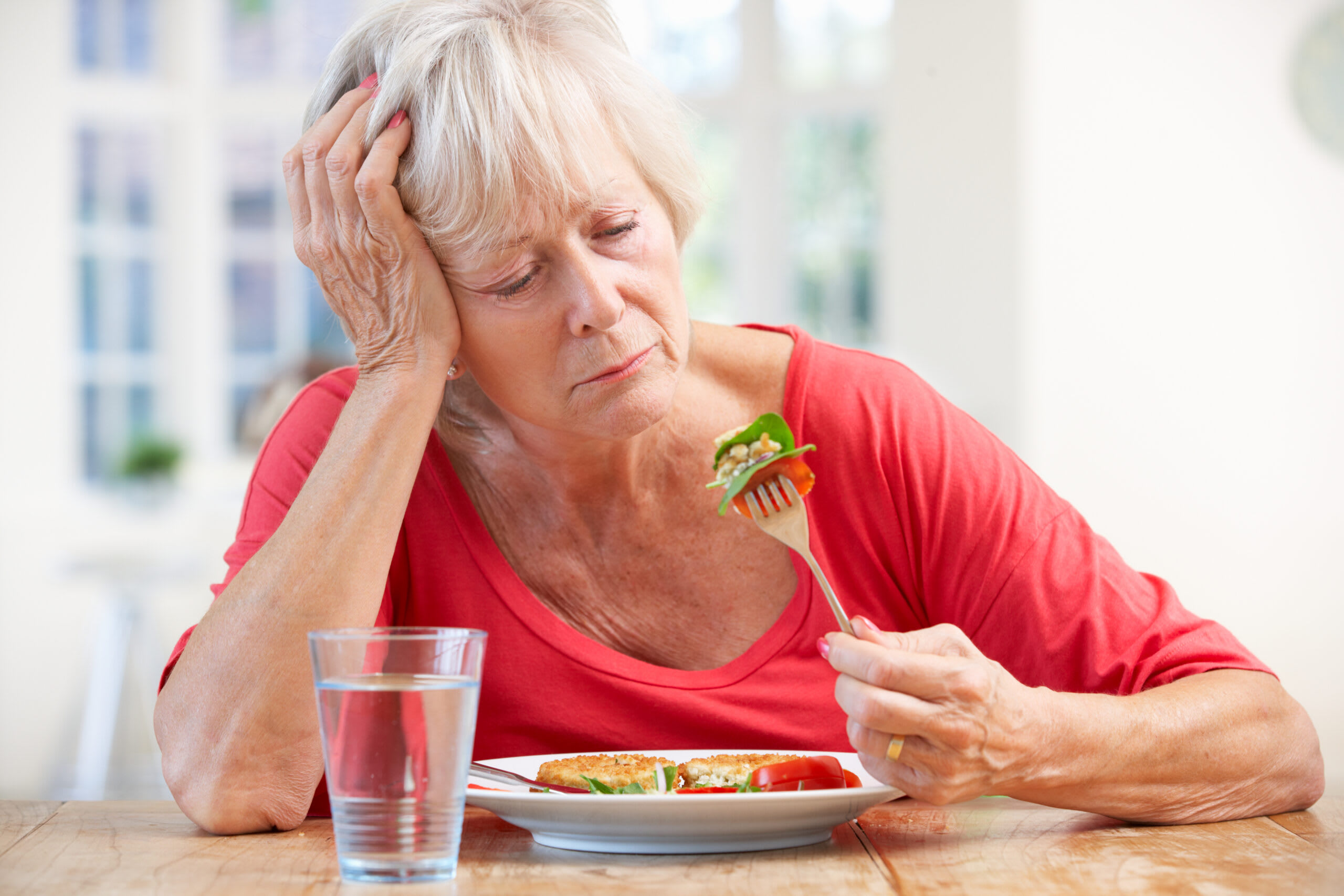 A senior woman in a pink shirt looks at her food.