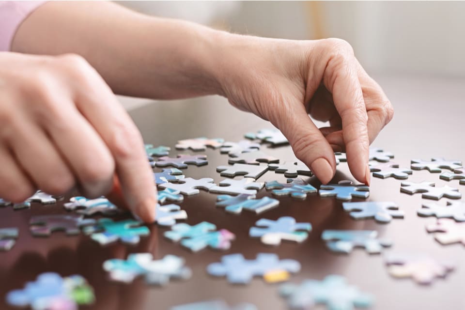 Two hands arrange puzzle pieces on a wooden table.