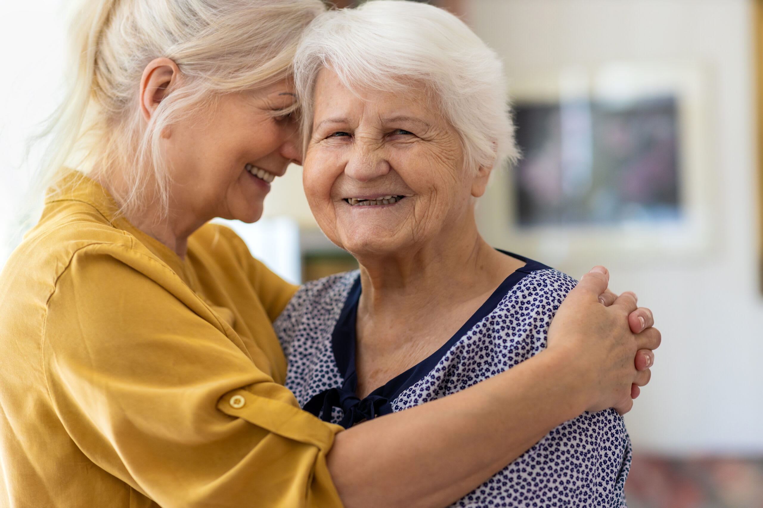 A woman hugs an elderly woman while smiling.