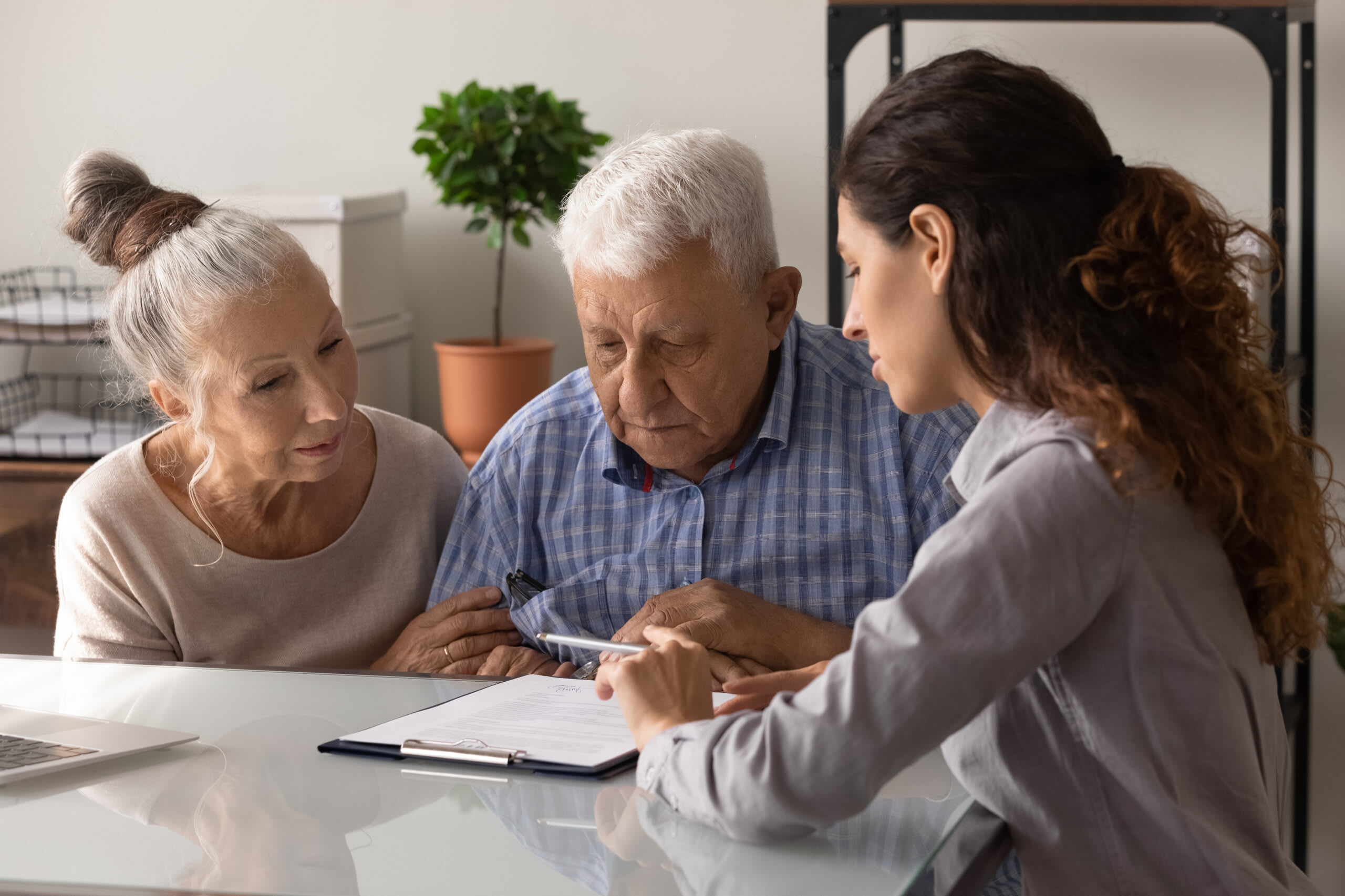 A senior man and woman sit at a table and discuss joint bank accounts with a young woman.