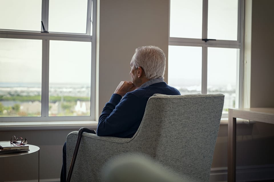 A senior man sits alone while staring out of a window.