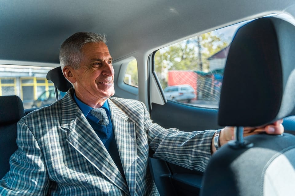 A senior man sits in the back of a car.