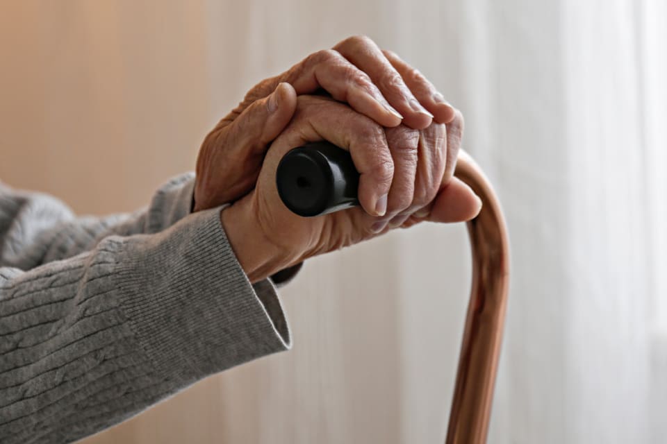 A senior woman with arthritis holds a cane.