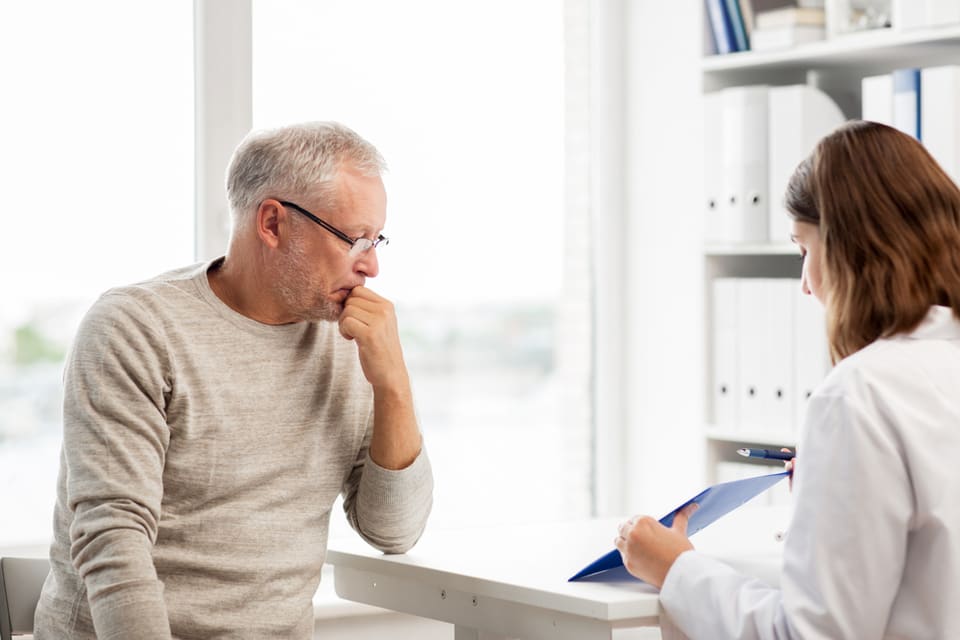 A senior man sits and speaks with a doctor.