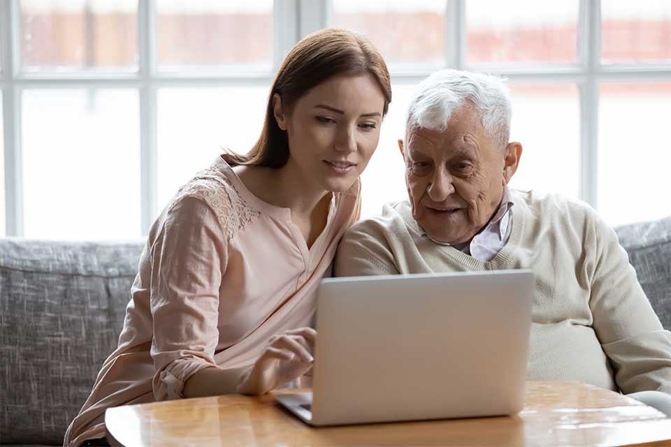 Elderly man and his daughter touring a senior living community on their laptop.