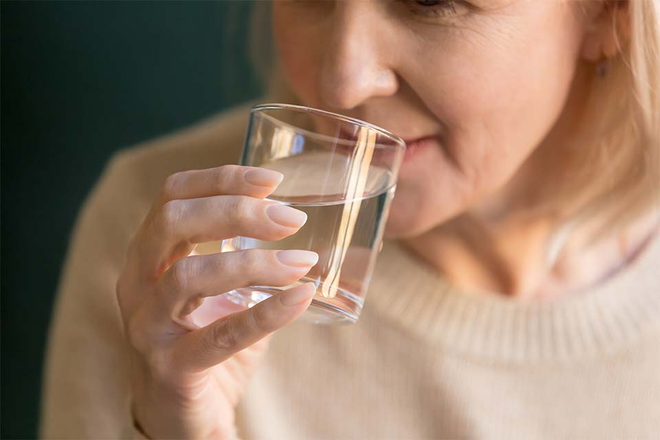 Elderly woman drinking water to flush out a urinary tract infection