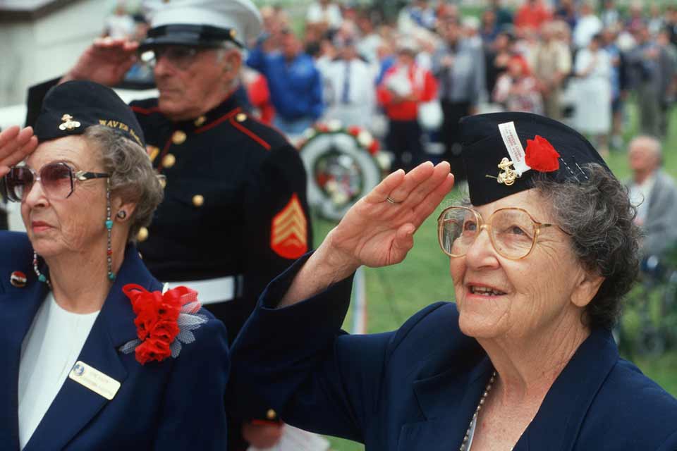 Two female veterans and a male veteran marine saluting a ranking officer at a group event.