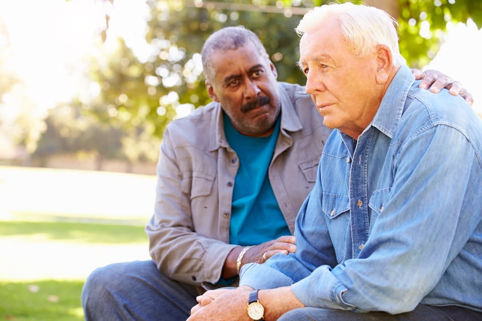 A friend consoles an elderly man whose partner has died.